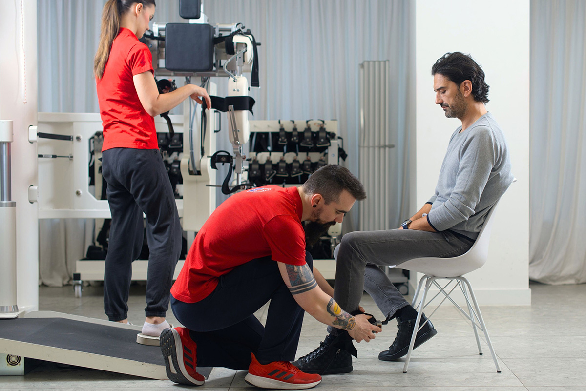 A therapist adjusts a leg support for a man seated beside a rehabilitation device.