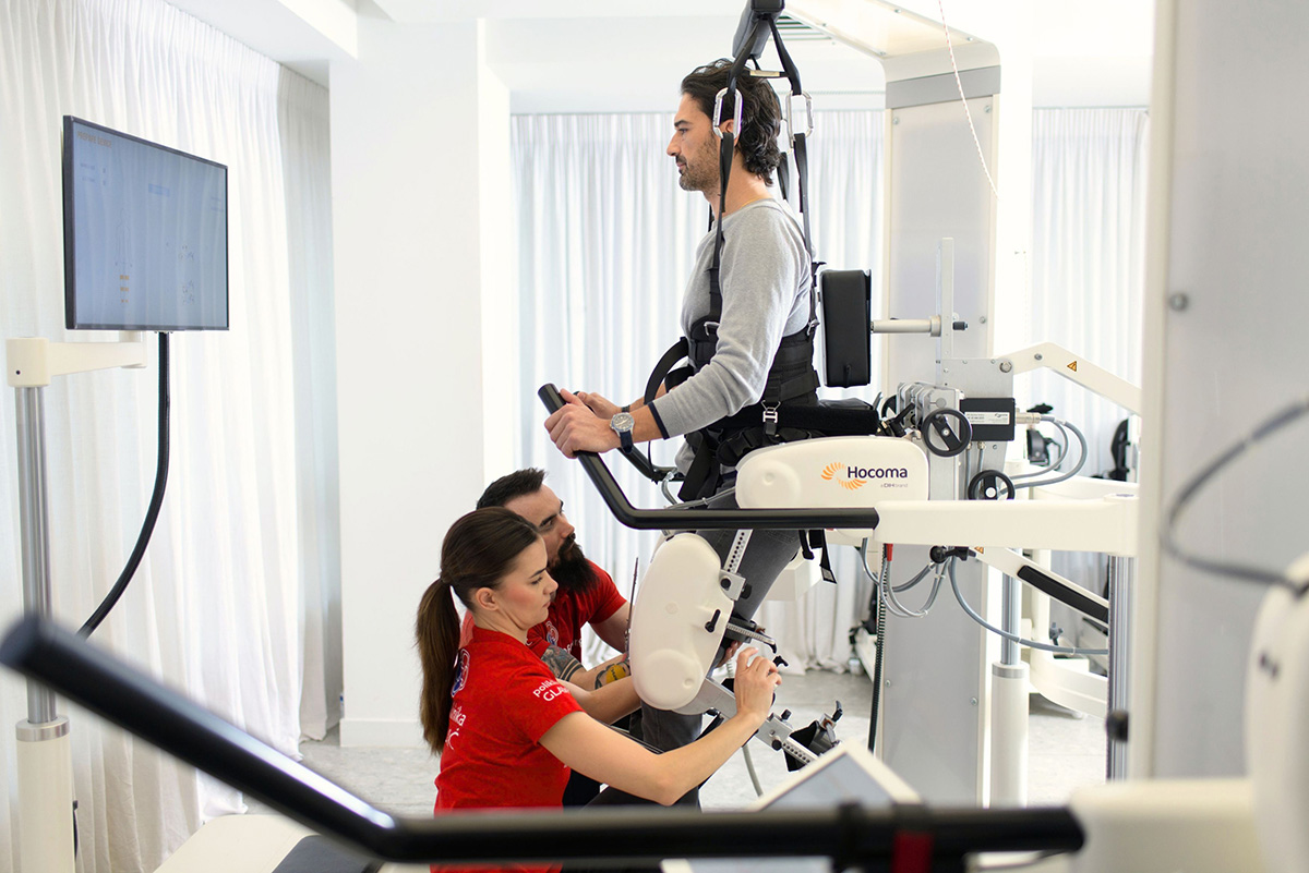 A female therapist adjusts a robotic gait training device beside a man on a treadmill.